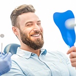 Man with beard smiling while looking into dental mirror
