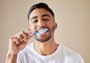 Man in white shirt smiling while brushing teeth