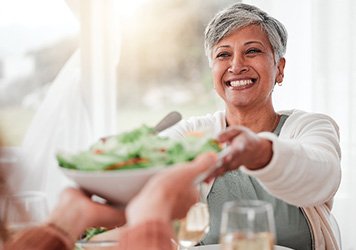 Smiling woman grabbing salad bowl across the table