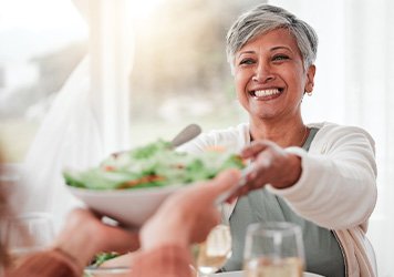 Woman with short gray hair smiling as salad is passed to her at the dinner table