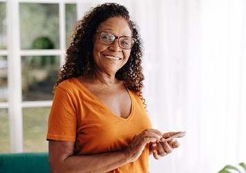 Senior woman with glasses smiling while looking at phone