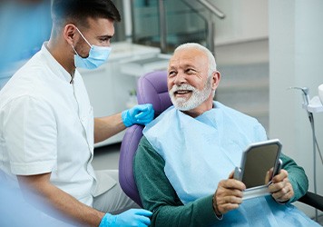 Senior patient looking at dentist while holding small mirror