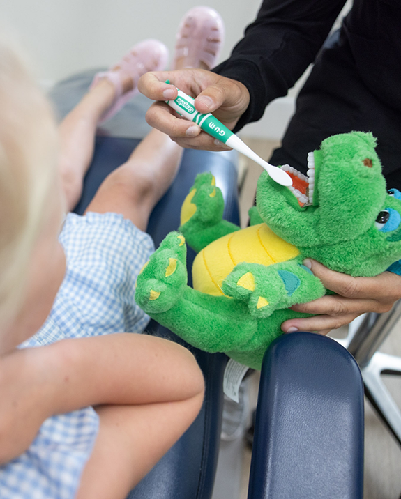 Dental team member demonstrating using a toothbrush on a plush crocodiles teeth during a childs dental appointment