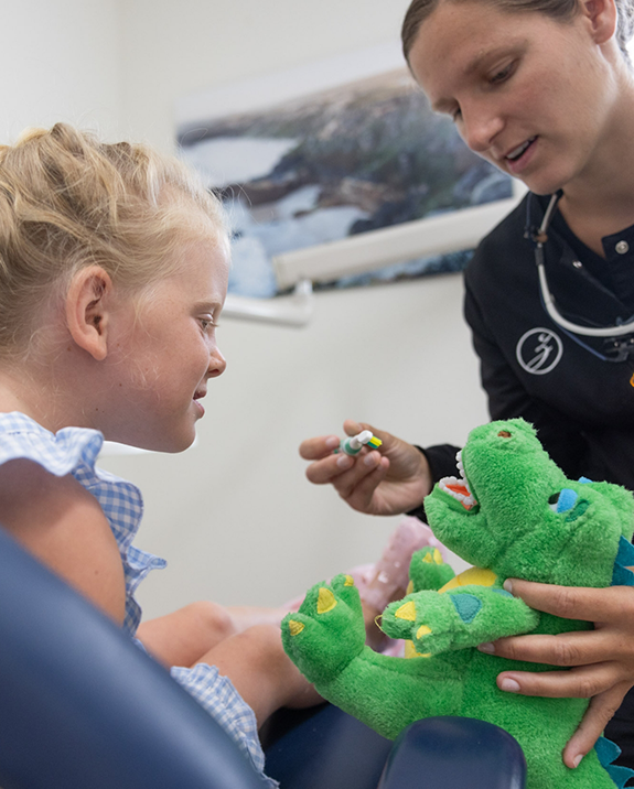 Young girl watching her childrens dentist in Ellington brush the teeth of a stuffed crocodile