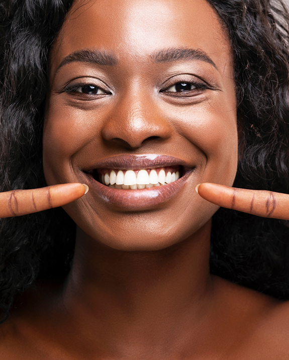 Woman with flawless teeth pointing to her smile after cosmetic dentistry in Ellington