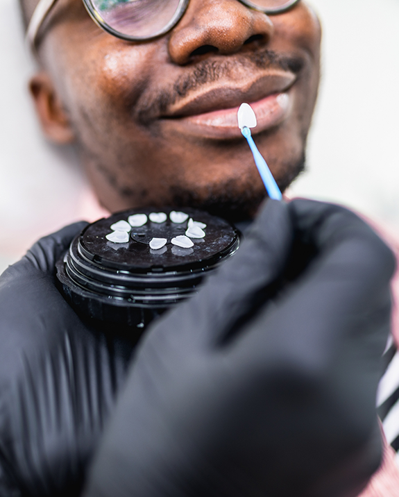 Cosmetic dentist holding a veneer in front of a smiling patient