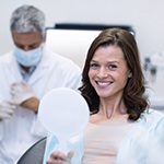 Woman visiting an implant dentist in Ellington while holding a mirror