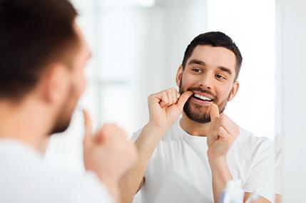 closeup of man flossing teeth in bathroom mirror