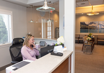 Dental team member at front desk smiling as she answers the phone