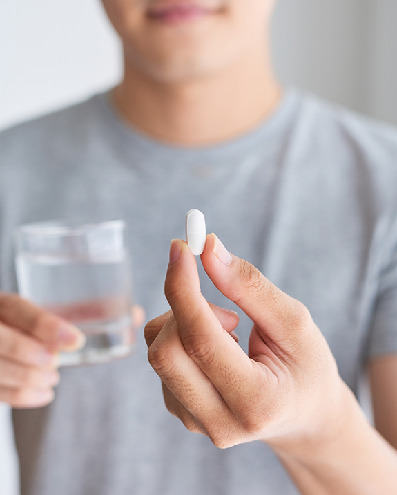 Person taking a white pill with a glass of water