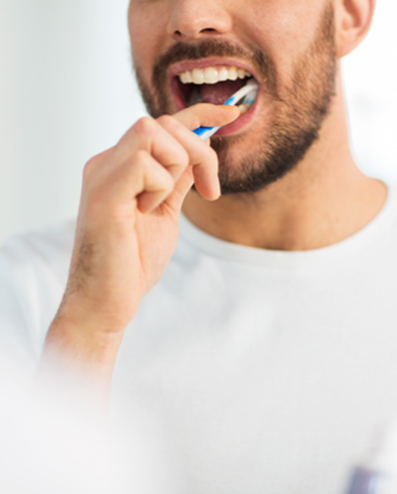 Man smiling while brushing his teeth