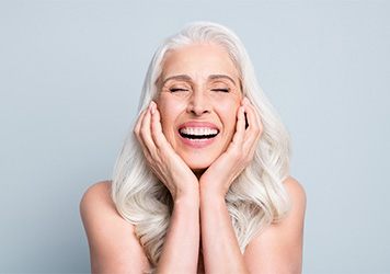 Woman white white hair smiling with eyes closed and holding hands to cheeks