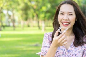 Smiling woman holds Invisalign in Ellington while travelling for summer