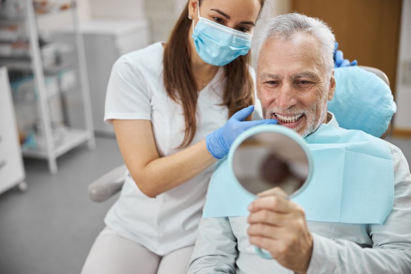 An older man admiring his new dental implants in a mirror
