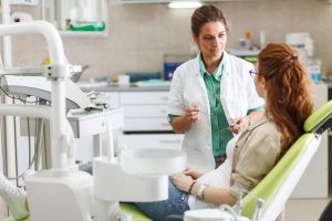 Female dentist in dental office talking with female patient and preparing for treatment.